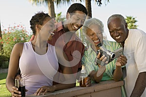 Senior couple and mid-adult couple looking at camcorder outdoors.