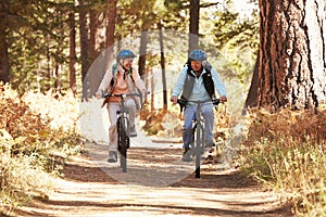 Senior couple mountain biking on forest trail, California