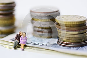 Senior couple with no money shortage, plastic figurine of two old citizens sitting on cash banknotes