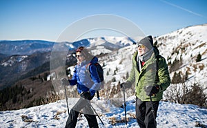 Senior couple with nordic walking poles hiking in snow-covered winter nature.