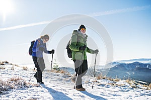 Senior couple with nordic walking poles hiking in snow-covered winter nature.