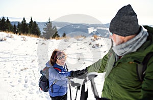 Senior couple with nordic walking poles hiking in snow-covered winter nature.