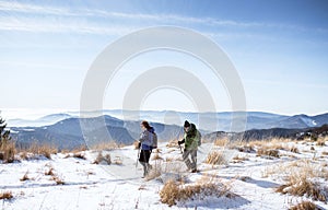 Senior couple with nordic walking poles hiking in snow-covered winter nature.