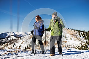 Senior couple with nordic walking poles hiking in snow-covered winter nature.