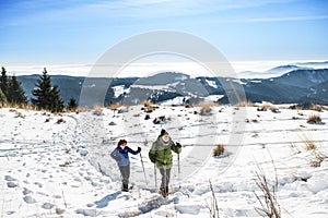 Senior couple with nordic walking poles hiking in snow-covered winter nature.