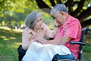 Senior couple in the park and wife taking care of a husband in a wheelchair a patient with paralysis, with his wife comforting and