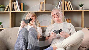 Senior couple playing video games online, holding game controllers, having fun together, sitting on the couch at home