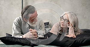 Senior couple reading book lying together on bed