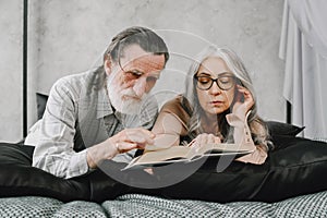 Senior couple reading book lying together on bed