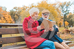 senior couple reading book while sitting on bench