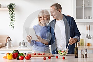 Senior couple reading food blog on digital tablet, cooking