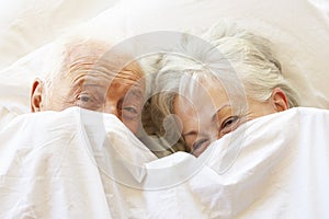 Senior Couple Relaxing In Bed Hiding Under Sheets