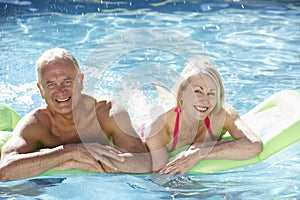 Senior Couple Relaxing In Swimming Pool On Airbed Together