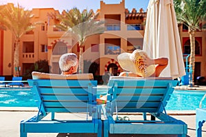 Senior couple relaxing by swimming pool lying on chaise-longues. People enjoying summer vacation.