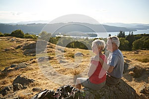 Senior Couple Resting At Top Of Hill On Hike Through Countryside In Lake District UK