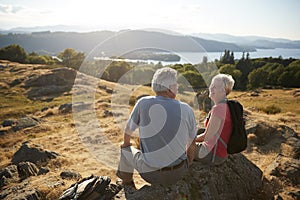 Senior Couple Resting At Top Of Hill On Hike Through Countryside In Lake District UK