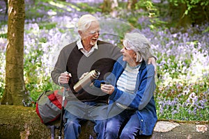 Senior Couple Resting On Walk Through Bluebell Wood