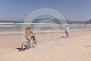 Senior couple riding bicycle on beach with mountains in the background