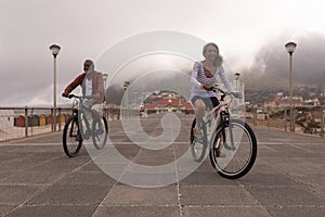 Senior couple riding bicycle on promenade with city in the background