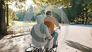 Senior couple riding double bicycle in autumn. Grandmother and grandfather cycling together . Elderly people healthy and