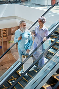 Senior couple riding down shopping mall escalator enjoying time together
