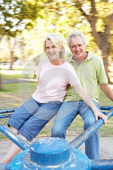 Senior Couple Riding On Roundabout In Park