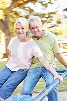 Senior Couple Riding On Roundabout In Park