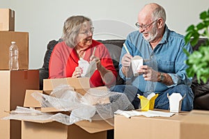 Senior Couple Sharing Chinese Food Surrounded By Moving Boxes