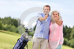 Senior couple showing OK sign on a golf course.