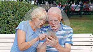 Senior couple sit on bench in park look for direction via online app with city map on mobile phone