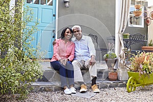 Senior couple sit on steps outside their house, full length