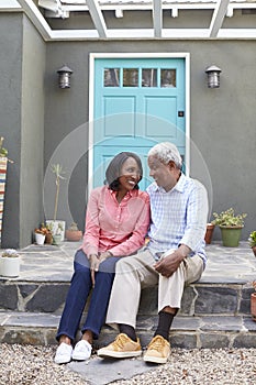 Senior couple sit on steps outside their house, vertical