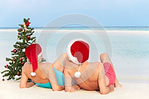 Senior Couple Sitting On Beach With Christmas Tree And Hats