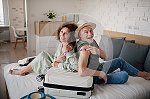 Senior couple sitting on bed indoors in hotel room, coronavirus vaccination, holiday and new normal concept.