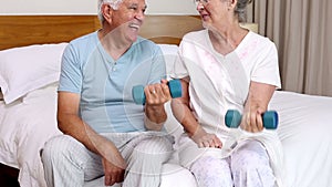 Senior couple sitting on bed lifting dumbbells