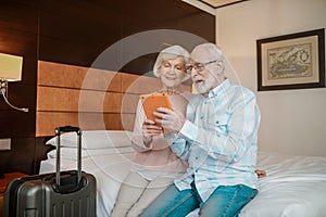 Senior couple sitting on a bed and watching something on a talet