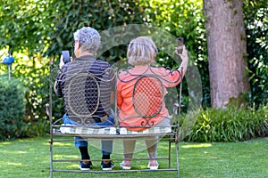 Senior couple sitting on bench with smartphones