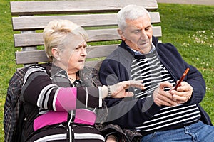 Senior couple sitting on bench struggling with mobile phone