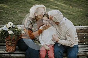 Senior couple sitting on the bench with their cute little granddaughter