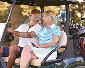 Senior Couple Sitting In Buggy On Golf Course Marking Score Card Together