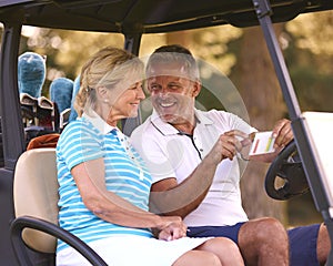 Senior Couple Sitting In Buggy On Golf Course Marking Score Card Together