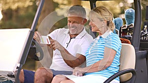 Senior Couple Sitting In Buggy On Golf Course Marking Score Card Together