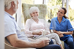 Senior Couple Sitting In Chair And Talking With Nurse In Retirement Home