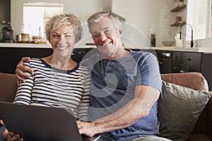 Senior couple sitting on couch use laptop, smiling to camera