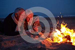 Senior Couple Sitting By Fire On Winter Beach