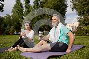 Senior couple sitting on fitness mats rest after yoga training outdoors in park