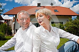 Senior couple sitting in front of their home