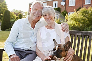 Senior Couple Sitting On Garden Bench With Pet French Bulldog