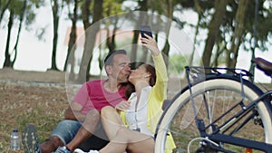 Senior couple sitting on grass in park and taking selfie