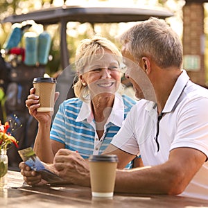 Senior Couple Sitting Having Coffee After Round Of Golf Looking At Score Card Together